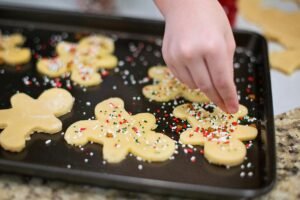 A close-up of gingerbread cookies being decorated with colorful sprinkles on a baking tray.