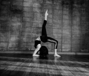 Black and white image of a woman performing a gymnastic pose indoors.