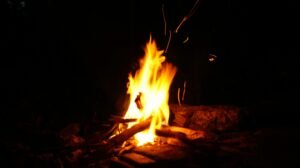 Close-up view of a campfire at night showing flames and sparks in a dark outdoor setting.