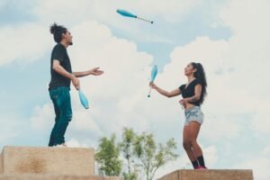 A couple performs an impressive juggling act outdoors against a backdrop of a bright blue sky.